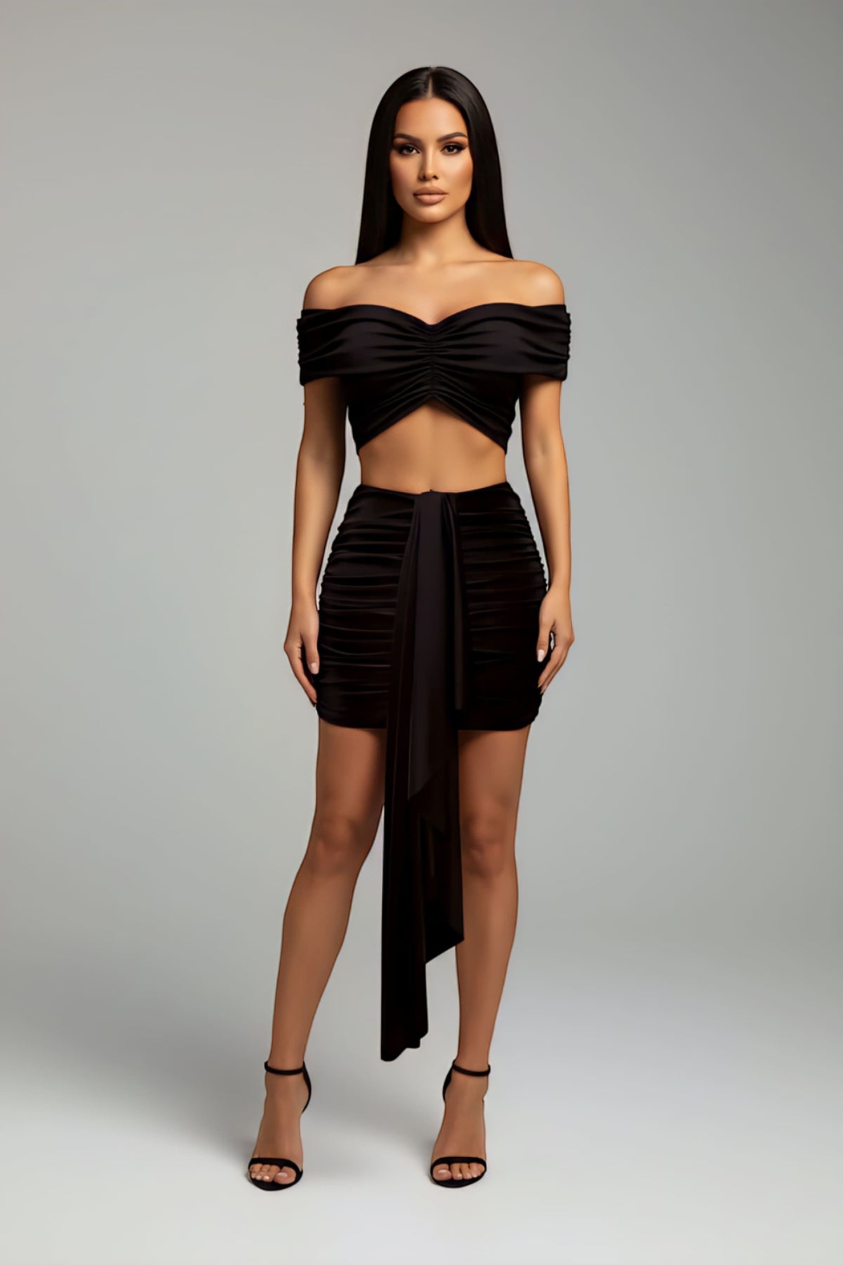 Model wearing The Saint 54 black two-piece set with off-shoulder cropped top and high-waisted mini skirt with drape detail